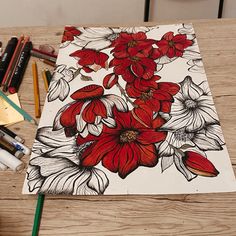 a drawing with red and white flowers sitting on top of a wooden table next to colored pencils