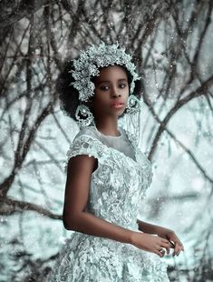 a woman in a white dress standing next to some trees with snow falling on it