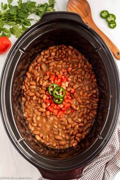 a slow cooker filled with beans and peppers next to some parsley on the side