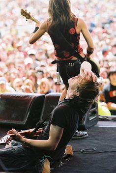 a woman sitting on the ground next to a man holding a guitar in front of an audience