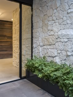 a planter filled with green plants sitting next to a stone wall on the side of a building