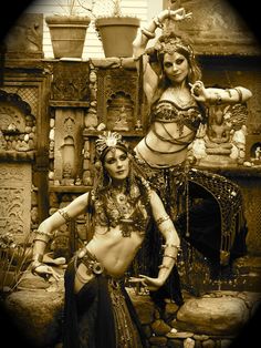 two women dressed in belly dance attire posing for the camera with pots and vases behind them