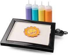 there is a black tray with markers and an orange sunflower on the bottom, next to it are four different colors of crayons