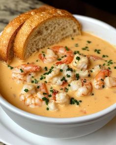 there is a bowl of soup with shrimp and bread on the side