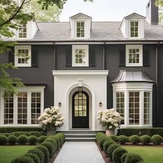 a large gray house with white trim and windows on the front door is surrounded by trimmed hedges