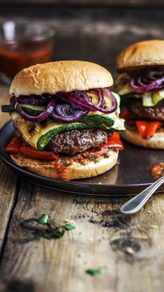 two hamburgers with onions and peppers on a black plate