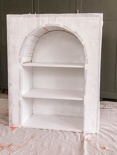 a white painted book shelf with an arch on the front and shelves in the back