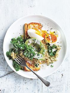 a white plate topped with eggs and rice next to a fork on a wooden table