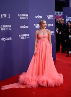 a woman in an orange dress standing on a red carpet with people watching from the sidelines