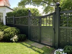 a large green fence in front of a house with bushes and flowers on the lawn