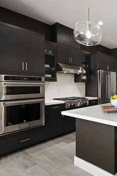 a modern kitchen with black cabinets and stainless steel appliances, marble counter tops, and an island in the middle