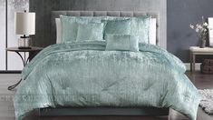 a bed with green comforters and pillows on top of it in a gray room