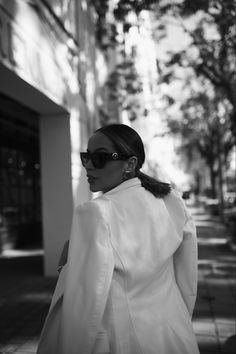 a woman walking down the street wearing sunglasses and a white coat with long sleeves on