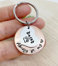 a hand holding a metal keychain with a heart and paw prints on it