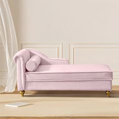 a pink velvet chaise lounger in front of a white wall and wooden floor