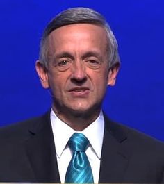 a man in a suit and tie standing behind a lectern with a blue background