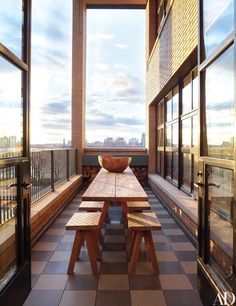 a long wooden table sitting on top of a tiled floor next to tall glass windows