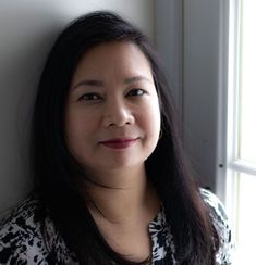 a woman standing in front of a window next to a white wall and wearing a black and white shirt