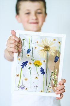 a young boy holding up a framed photo with wildflowers