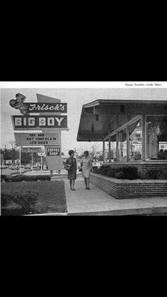 an old black and white photo of people walking in front of a big boy store