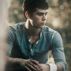 a young man sitting down with his hands on his knees and looking off into the distance