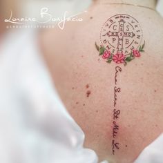 the back of a woman's shoulder with a cross and flowers tattooed on it