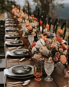 a long table is set with black and white plates, silverware, and orange flowers