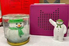 there is a snowman in a glass jar next to a speaker and a small figurine