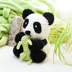 a small crocheted panda bear holding a green plant