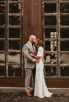 a bride and groom are kissing in front of an old building with large windows on the side