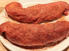 two pieces of meat sitting on top of a white plate with seasoning sprinkles