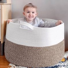 a small child is sitting in a large round basket on the floor and smiling at the camera