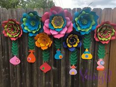 colorful paper flowers are hanging on a fence