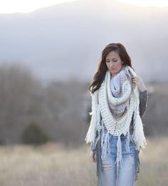 a woman standing in a field with a scarf around her neck and wearing ripped jeans