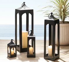 three black lanterns sitting on top of a wooden floor next to a potted plant