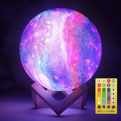 the colorful moon lamp is lit up on a wooden stand with remotes next to it