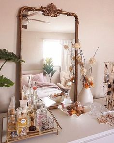 a mirror and some bottles on a white table in front of a bed with flowers