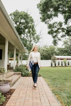 a woman walking down a brick walkway in front of a house