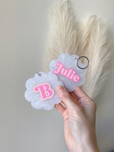 a person holding two personalized tags in front of a fake white feather wall with the letter b on it