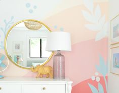 a white dresser topped with a mirror next to a pink and blue flowered wall