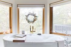 a large white bath tub sitting in a bathroom next to two windows with wreaths on them