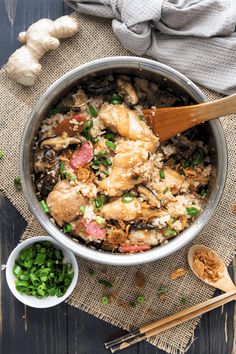 a pan filled with chicken and rice next to some green onions on a wooden table