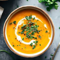 a bowl of carrot soup with sour cream and parsley in the center on a gray surface