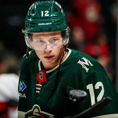 a hockey player wearing a green jersey and holding a stick in front of his face