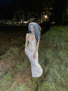 a woman with blue hair wearing a white dress and veil in the grass at night