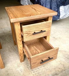 a wooden table with two drawers sitting on the floor next to a bed in a room