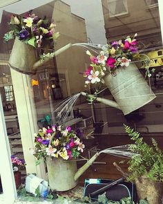 three buckets filled with flowers sitting on top of a window sill in front of a store