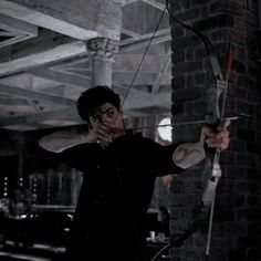 a man holding a bow and arrow while standing in front of a brick wall,