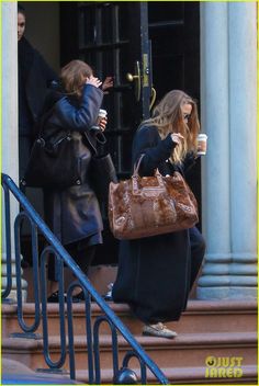 two women are walking down the steps with coffee in hand and one is on her cell phone