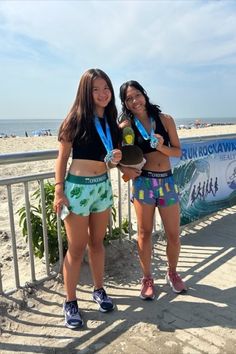 two women standing next to each other with medals in their hands and one holding a surfboard